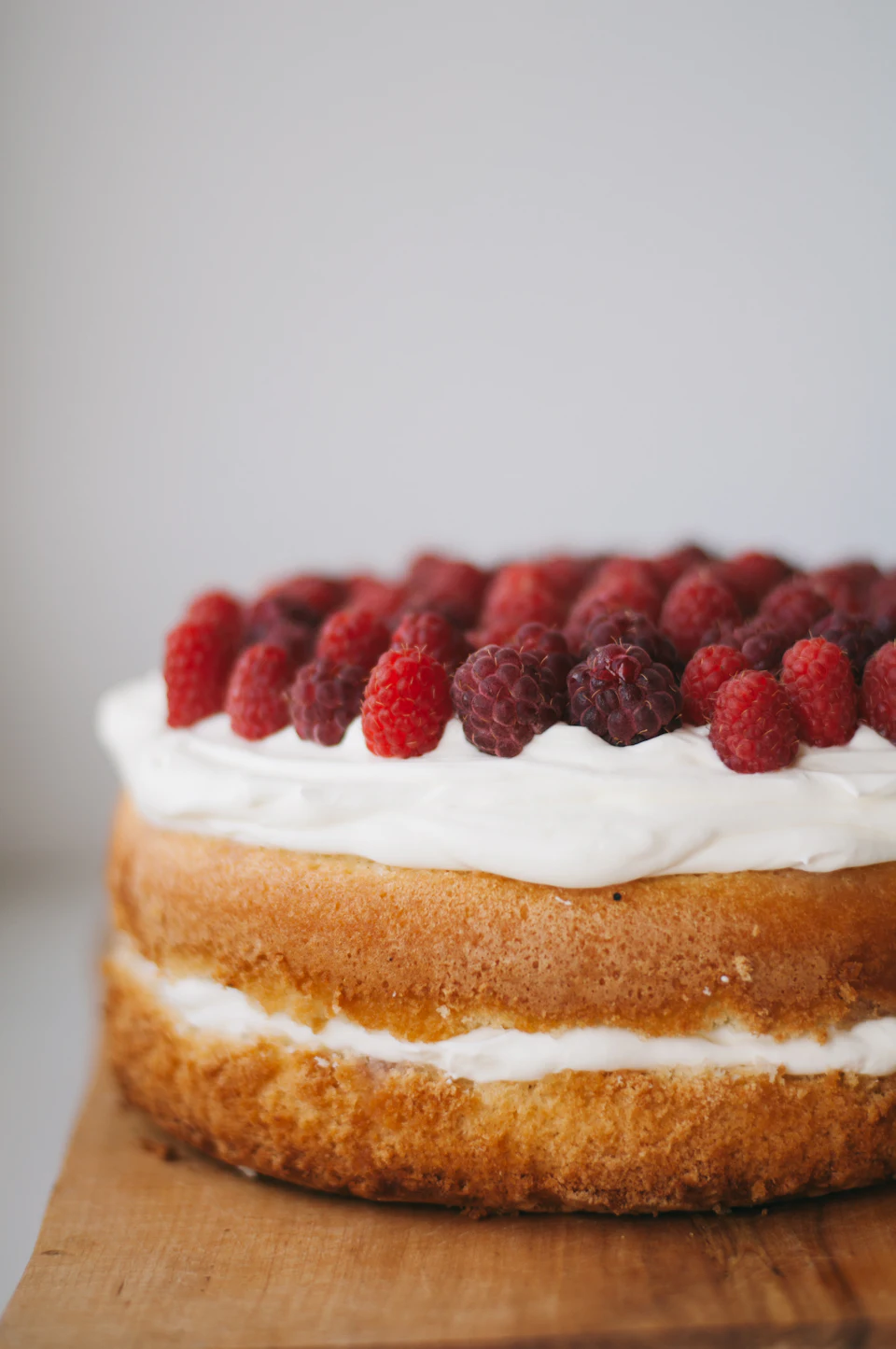 Round cake with white frosting topped with red raspberries
