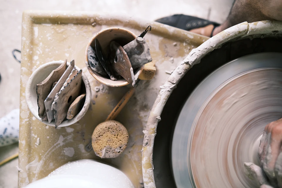 A person shaping clay on a spinning pottery wheel with tools in nearby bowls