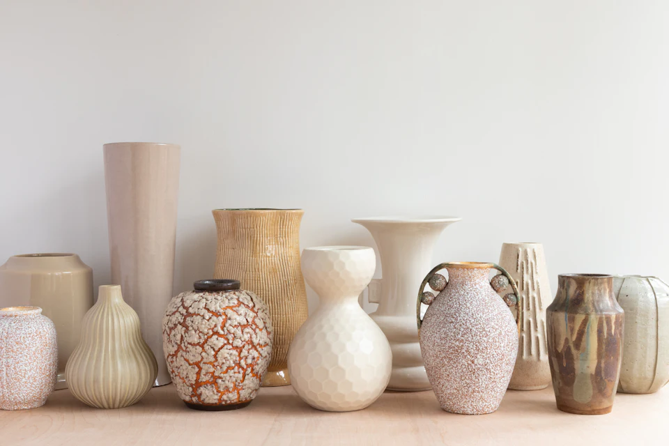 A collection of various ceramic vases in neutral tones on a wooden surface