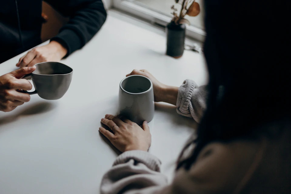 Two people holding gray mugs at table