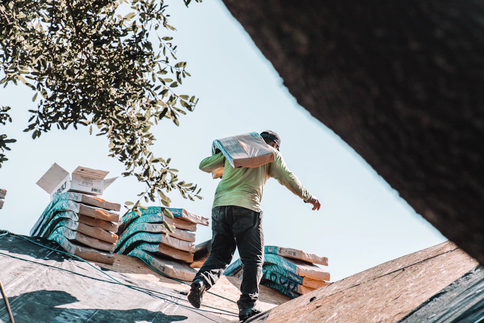 A person carrying a bundle of shingles across a residential roof