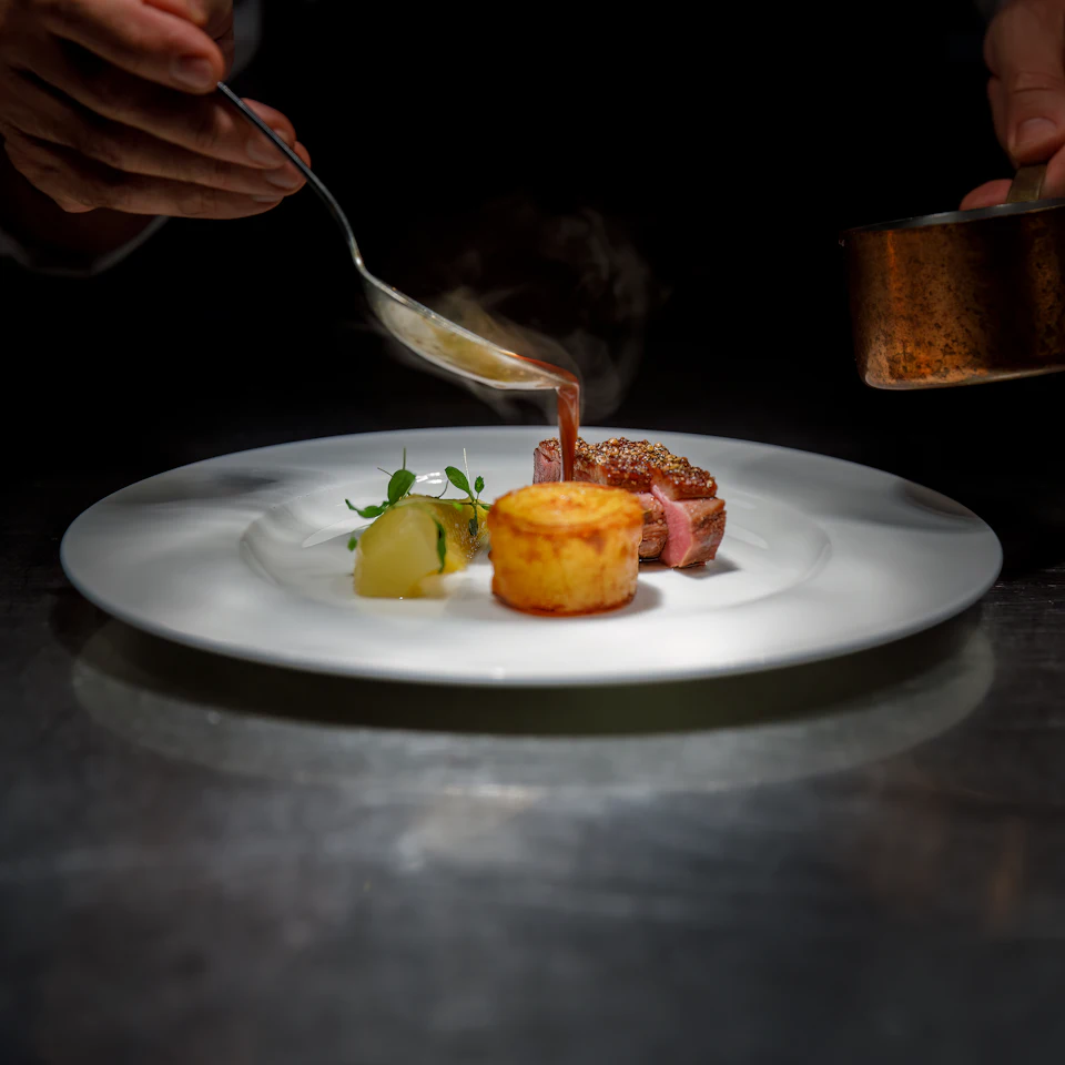 Chef pouring sauce over plated steak