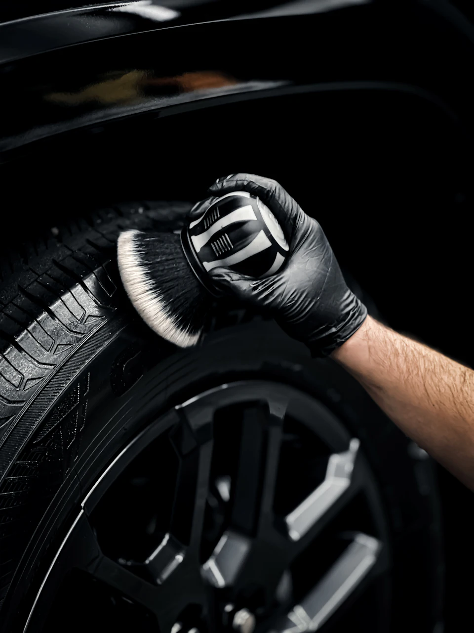 A person in a black glove cleaning a car tire with a brush