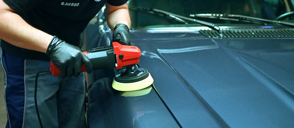 Person polishing a blue car's hood with an orbital buffer