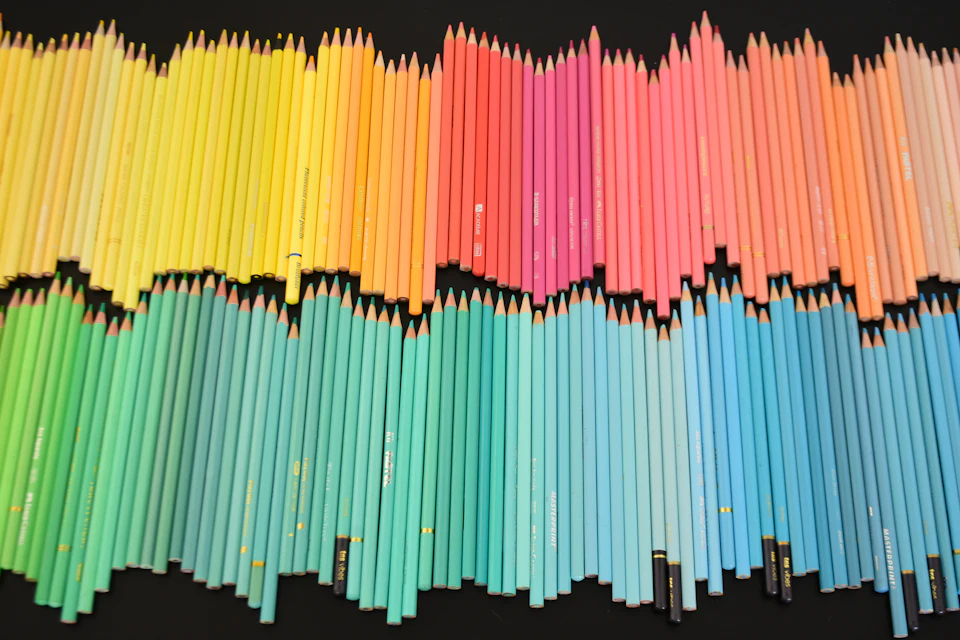 A large collection of colored pencils arranged in a spectrum on a black background
